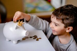 3 to 5 year old little boy putting coins into a piggy bank
