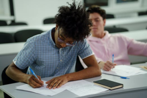 Two 14 to 18 year old boy students focused on studying and writing notes in a classroom.